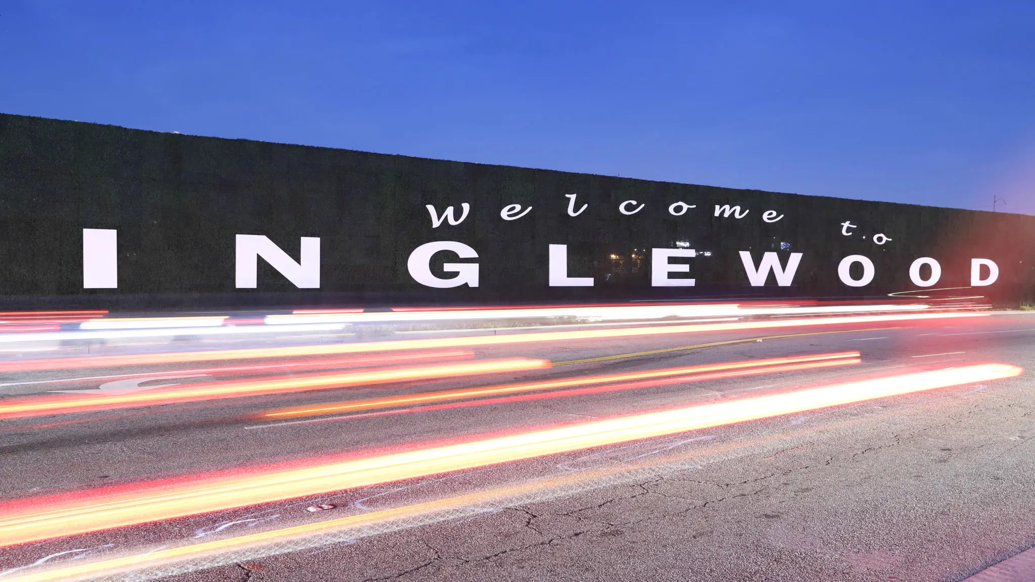 Light trails pass a welcome sign for Inglewood at night.