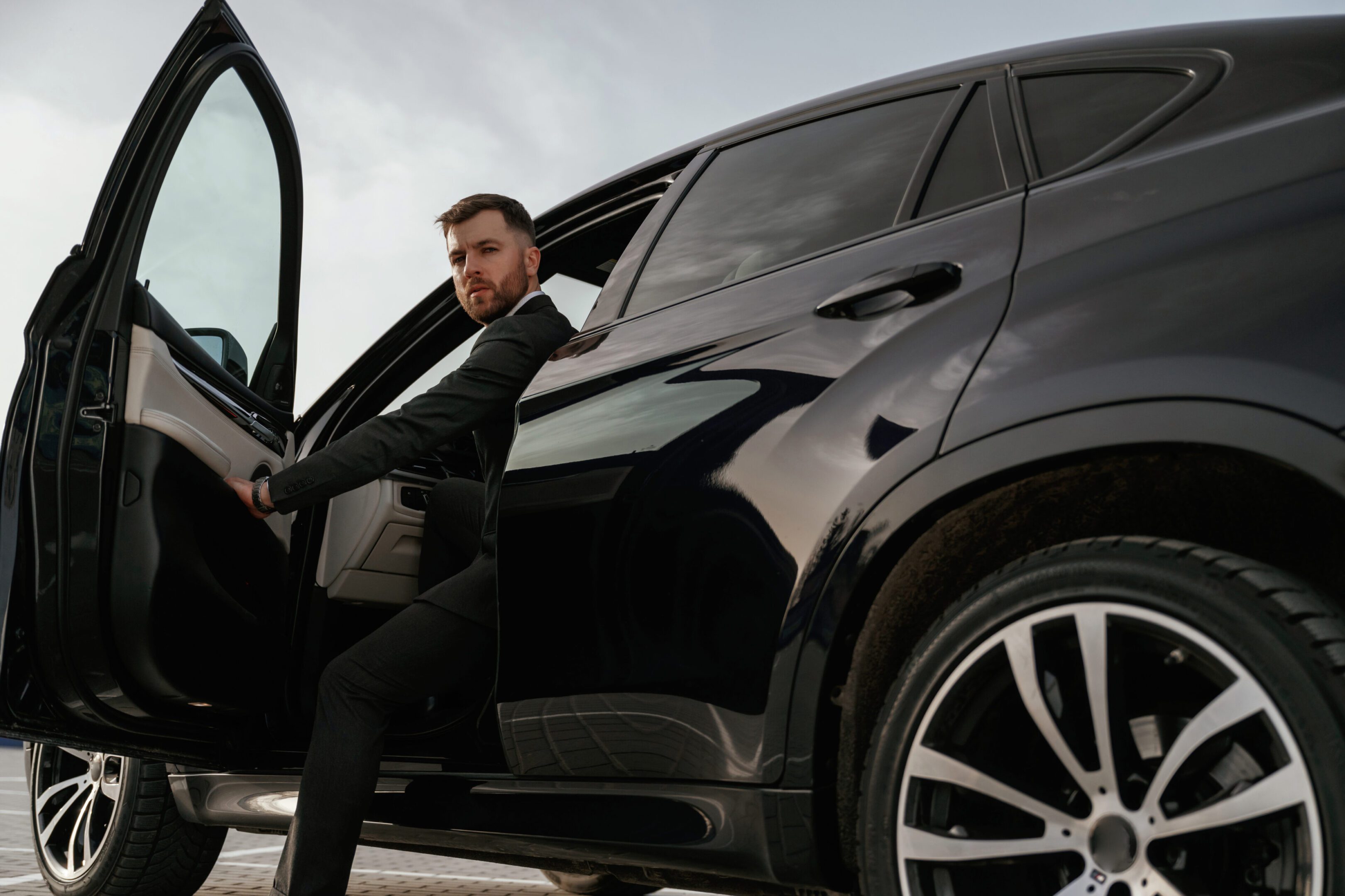 Man stepping out of a black luxury SUV looking confident.
