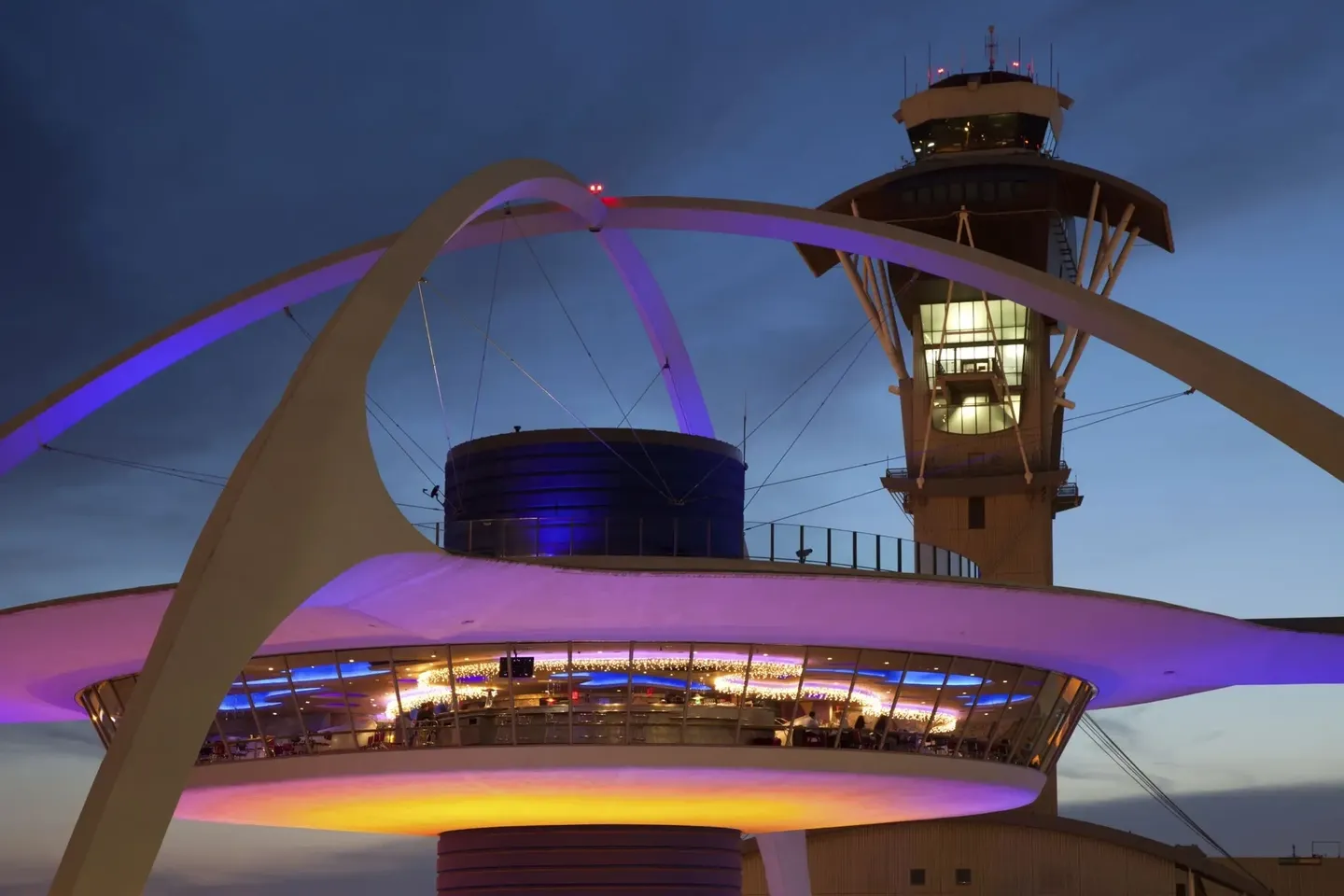 Night view of the iconic Theme Building at LAX with purple lighting.