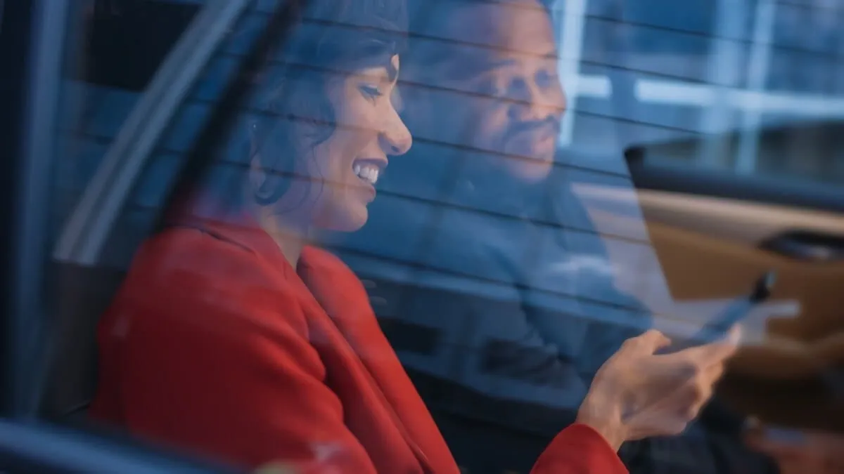 A smiling woman and a man looking at a phone inside a car.