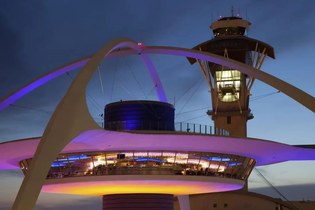 Night view of the iconic Theme Building at LAX with purple lighting.