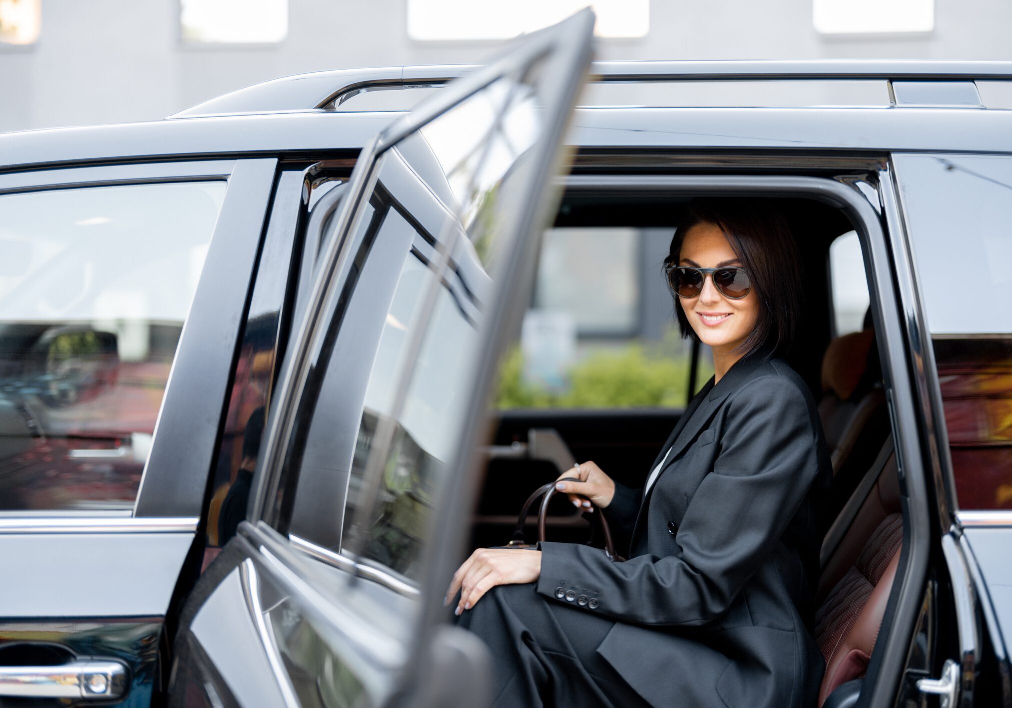 Woman in sunglasses sitting in a car with the door open.
