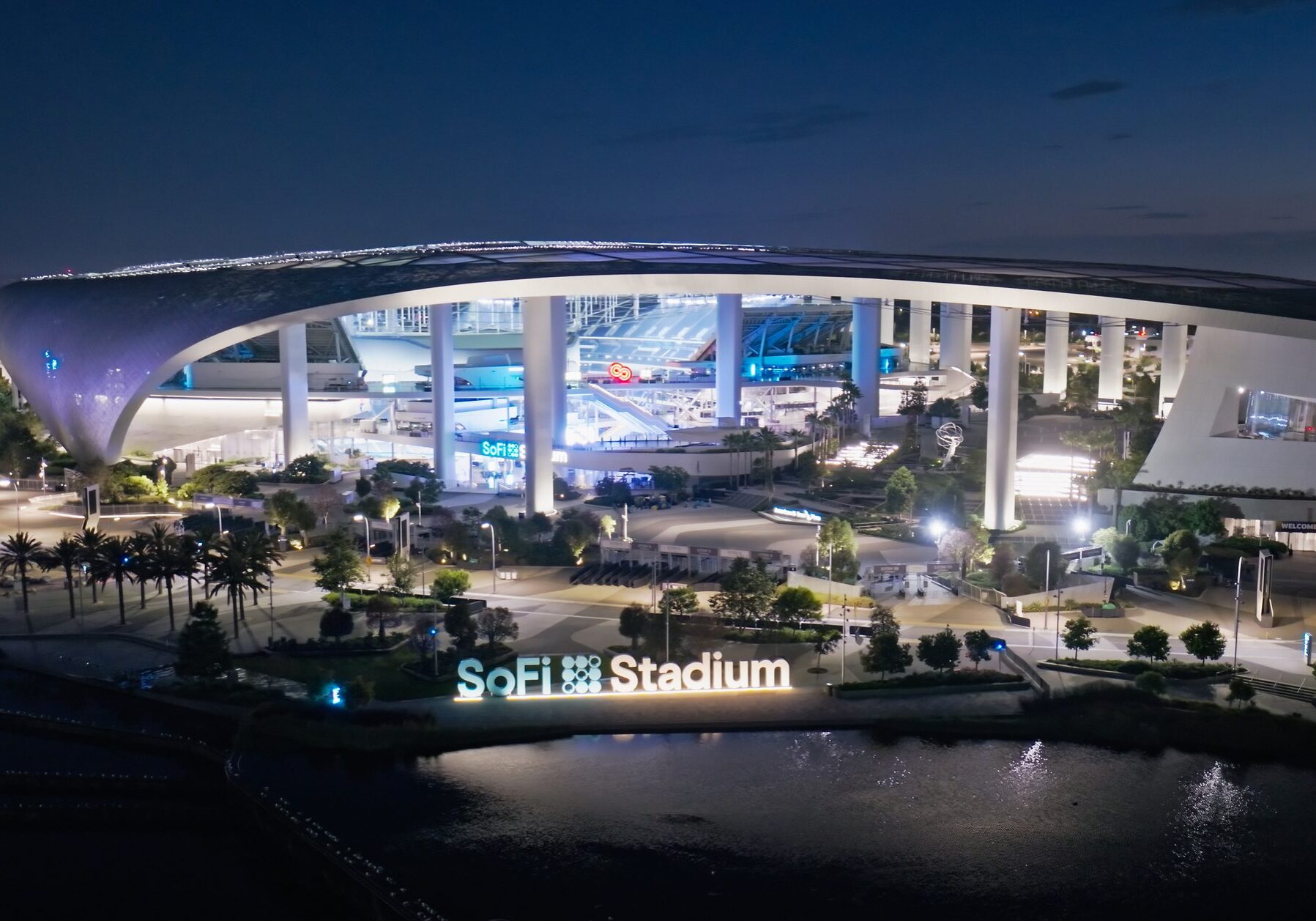 Night view of SoFi Stadium illuminated with blue and white lights.