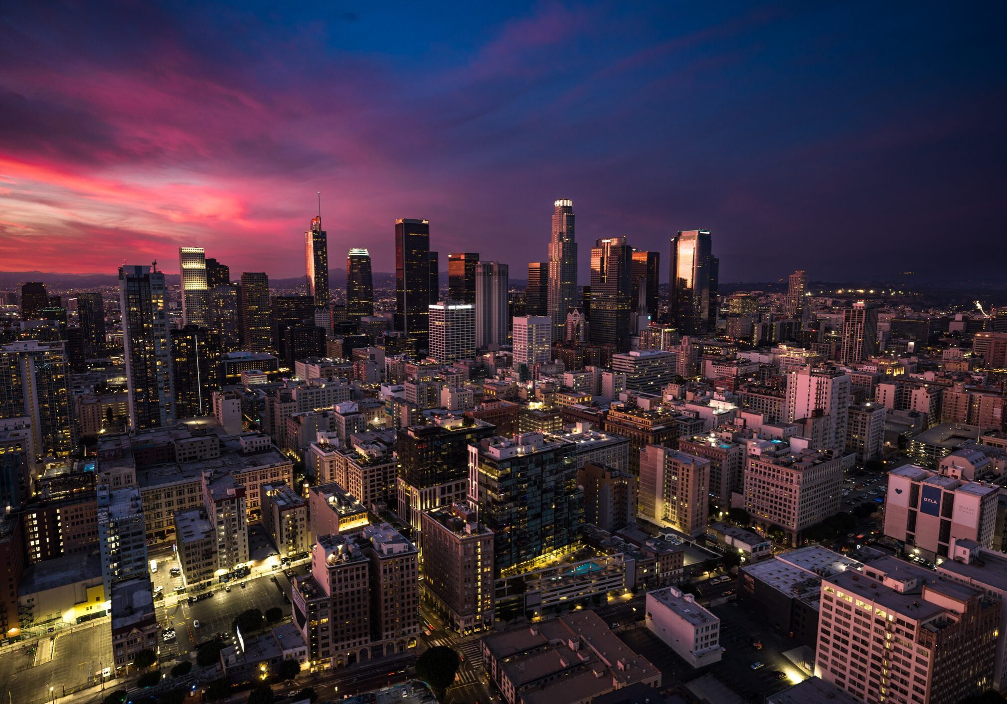 City skyline at dusk with vibrant sunset colors and illuminated buildings.