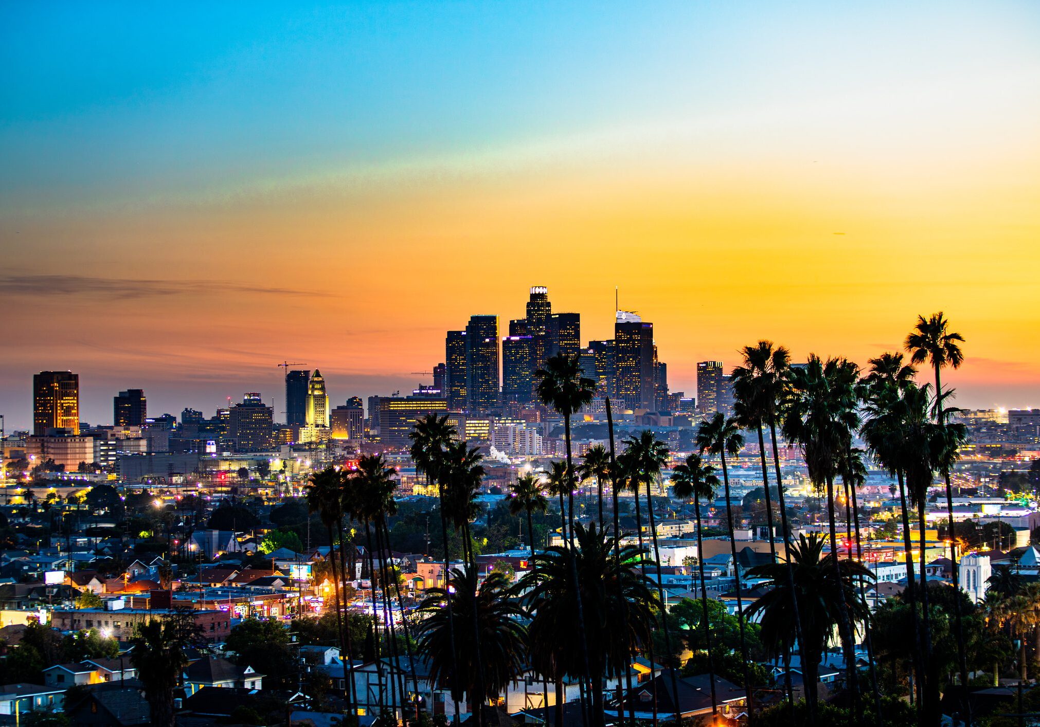 City skyline at sunset with palm trees and colorful sky.
